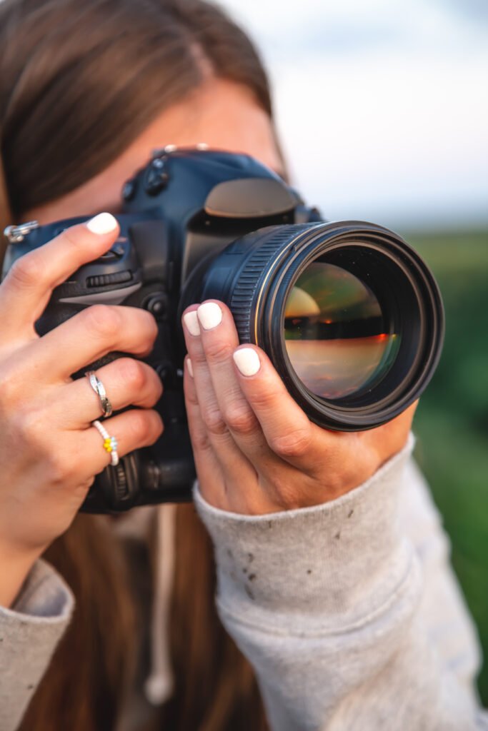 "A young woman photographer with a professional camera takes a photo in nature, close-up."